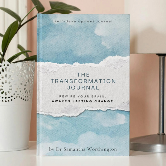 Book titled 'The Transformation Journal' on a surface with a lamp and plant in the background. Dr Samantha Worthington